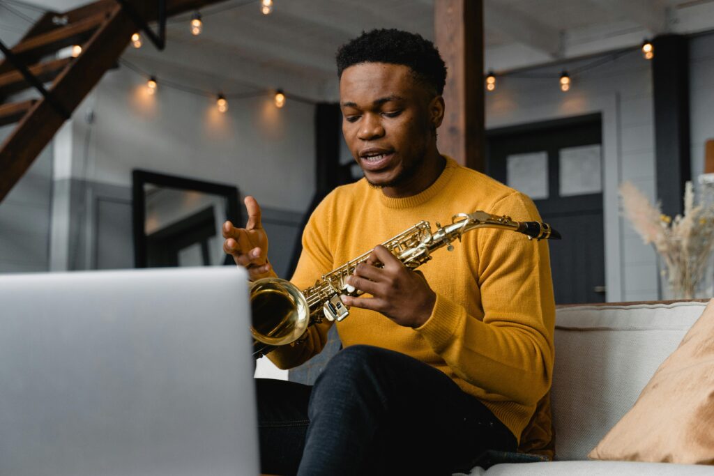 Young man with saxophone conducting an online music session from home.